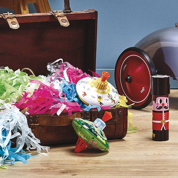 Colourful spinning top toys, ribbons and decorations in an open suitcase with a blue wall background