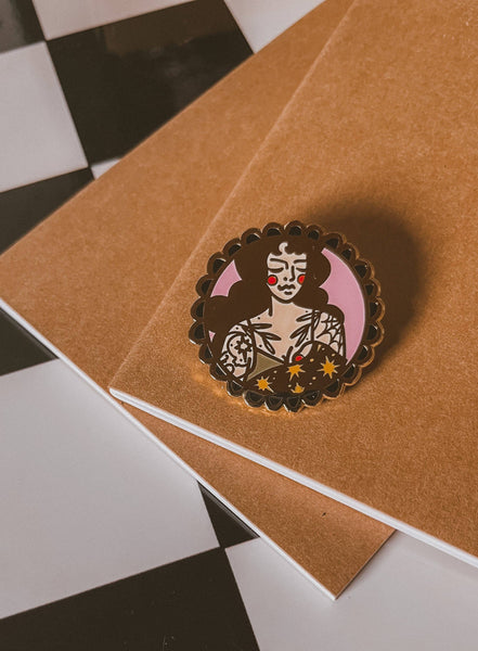 Enamel pin with a stylized portrait on a brown surface