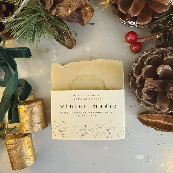 Winter Magic soap in a cardboard sleeve on a grey surface surrounded by berries and pinecones.