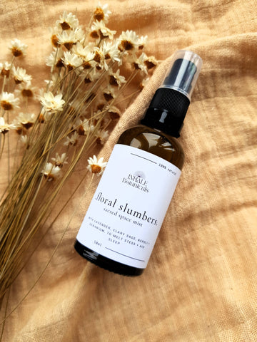 Bottle of 'Floral Slumbers' space mist on a wooden surface with dried flowers.
