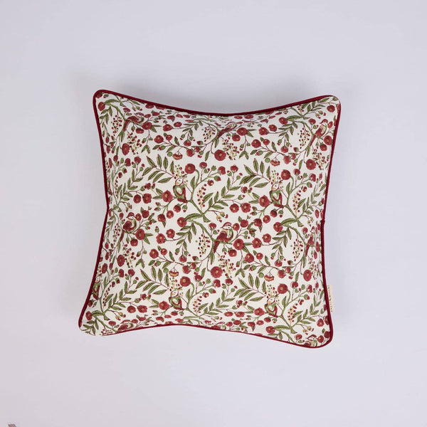 A square decorative throw pillow with a cream background, an all-over red berry and green leaf botanical pattern, and a contrasting dark red piped edge, shown against a plain light grey background.