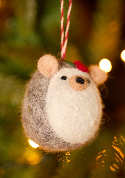 Felted hedgehog ornament, hanging on a string with a blurred Christmas tree background.
