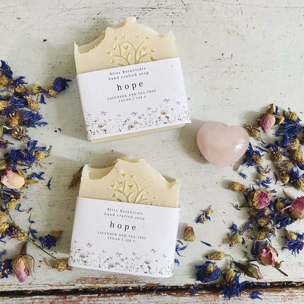 Two bars of 'hope' soap with floral packaging on a rustic surface with dried flowers.