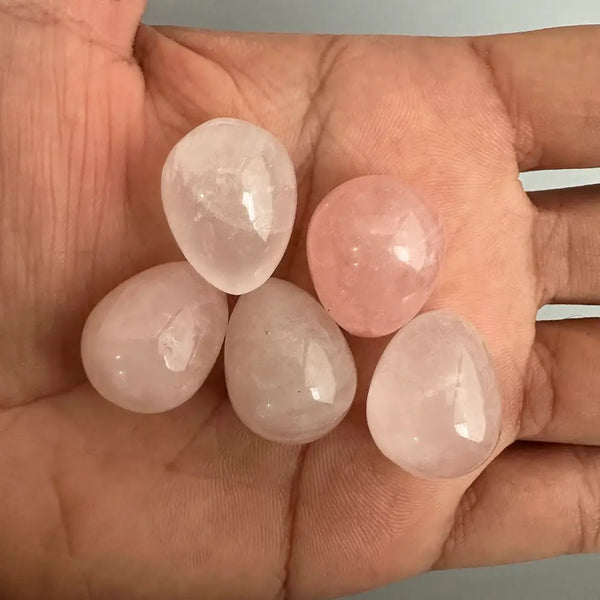 Five pink gemstones held in a hand against a neutral background