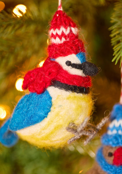 Knitted bird ornament with a red hat and blue scarf on a Christmas tree.