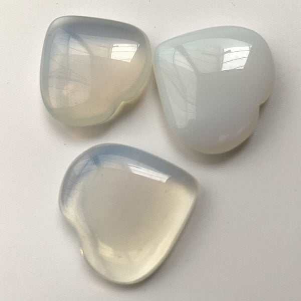 Three polished heart shaped moonstone crystals on a light grey background
