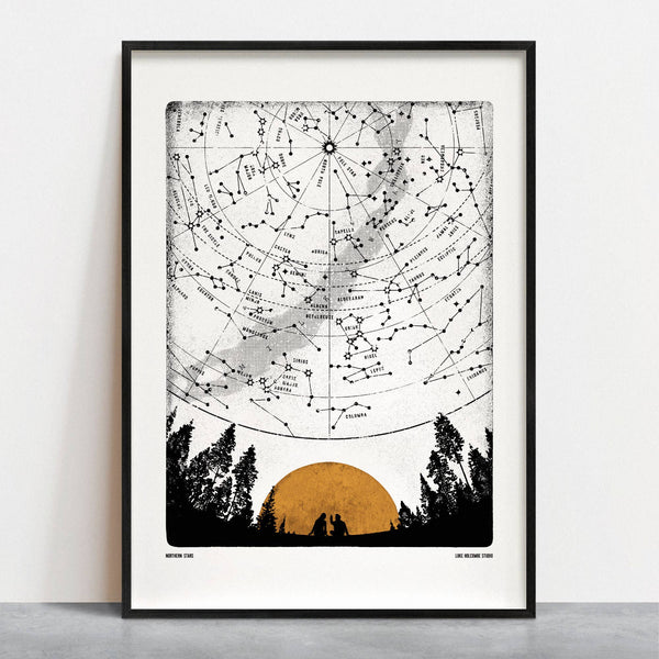 Framed star map with silhouette of trees and sunset on a white wall.