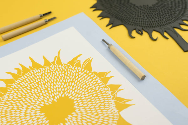 Yellow sunflower design on paper with carving tools on a yellow background