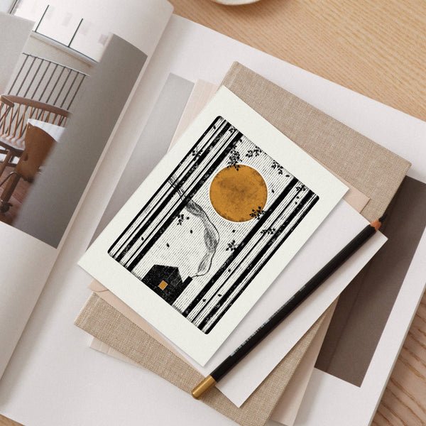 Greeting card with a stylized illustration of a house and sun on a table.