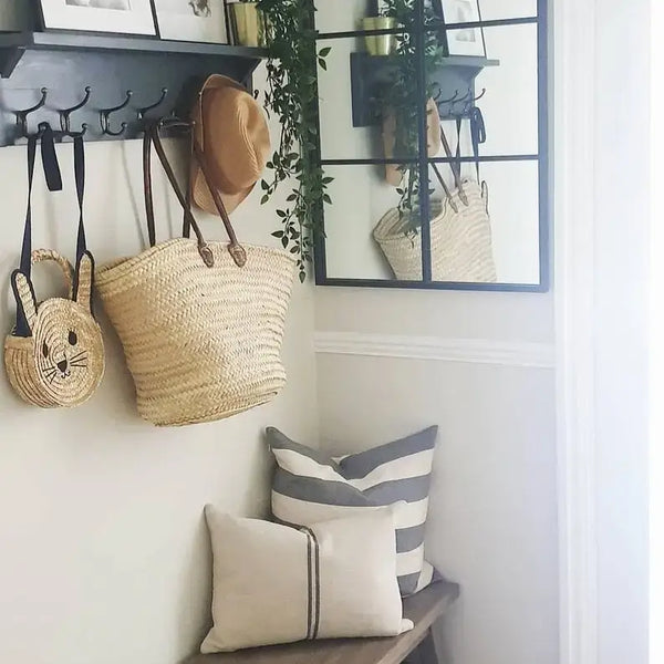 Entryway with bags hanging on a hook, mirror, and pillows on a bench.