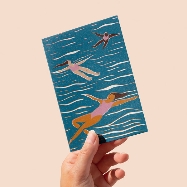 Hand holding a card with swimmer illustrations on a blue background