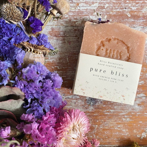 Bar of soap labeled 'pure bliss' with dried flowers on a wooden surface