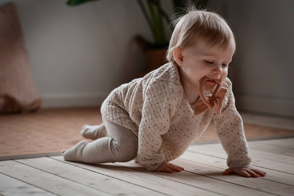 Baby in a beige outfit crawling on a wooden floor