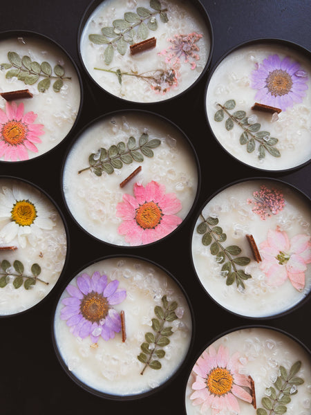 Candle tins with floral and leaf decorations on a black background