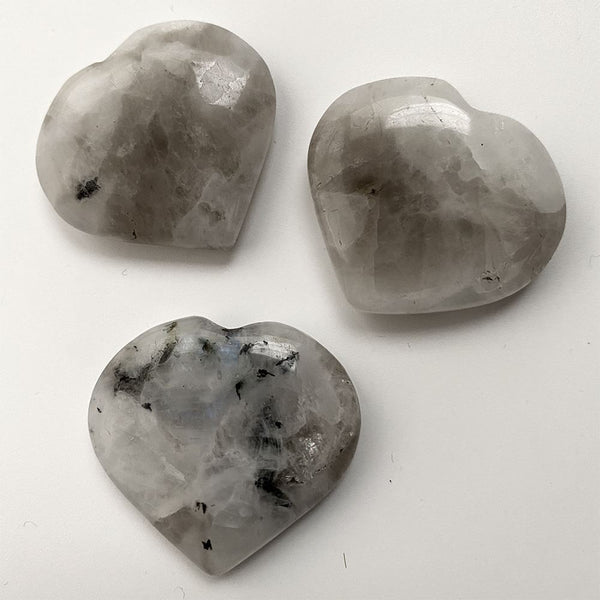 Three heart-shaped rainbow moonstone crystals on a white background
