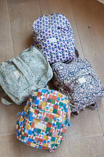 Four patterned backpacks on a wooden floor.