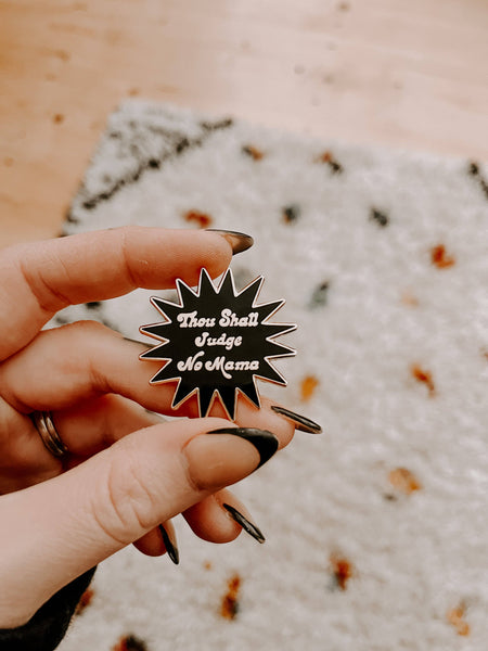 Person holding a star-shaped enamel pin with text against a textured surface.