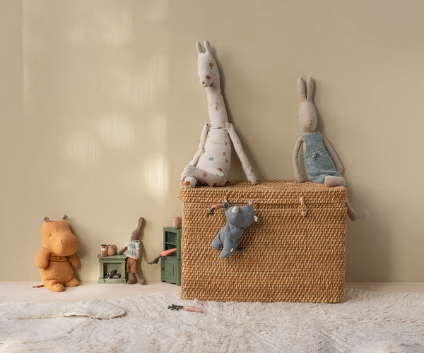 Wicker basket with plush toys on a light-coloured floor against a beige wall