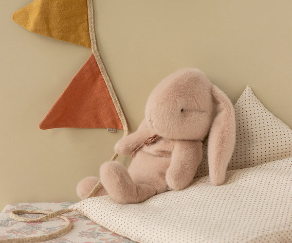 Pink plush bunny sitting on a cushion with bunting hanging down