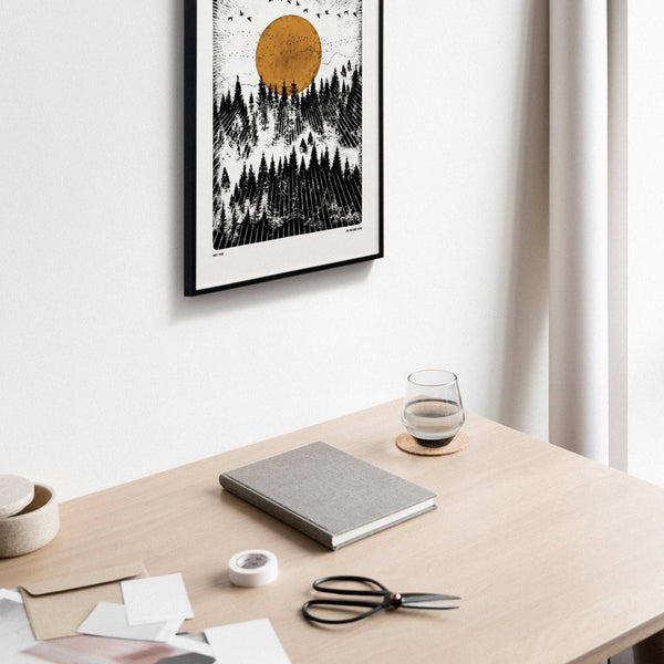 Desk with a notebook, scissors, and glass of water, framed artwork on the wall.
