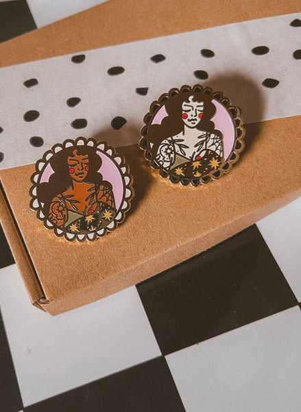 Two decorative pins with intricate designs on a brown box.