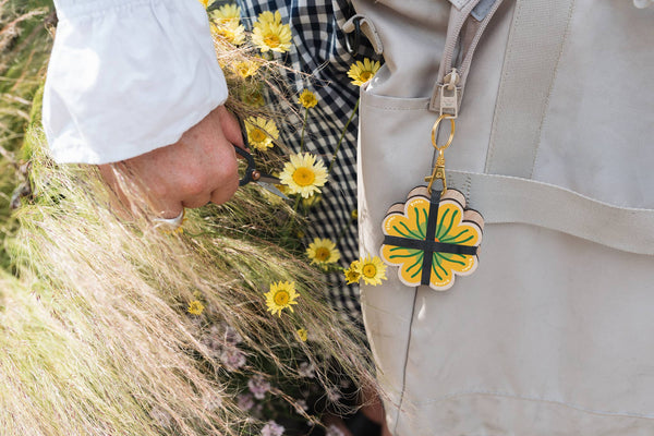 Person cutting a yellow flower with a floral  shaped mini flower press keychain attached to a beige bag.