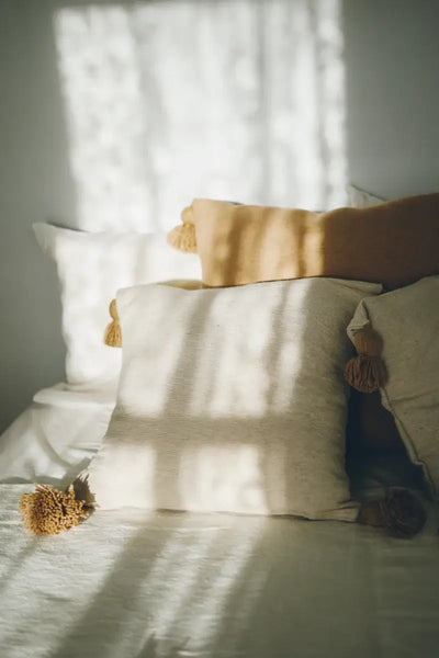 Cushions on a bed with sunlight filtering through curtains