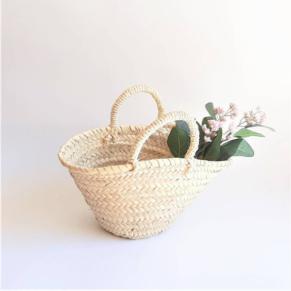 Woven basket with handles holding flowers on a white background