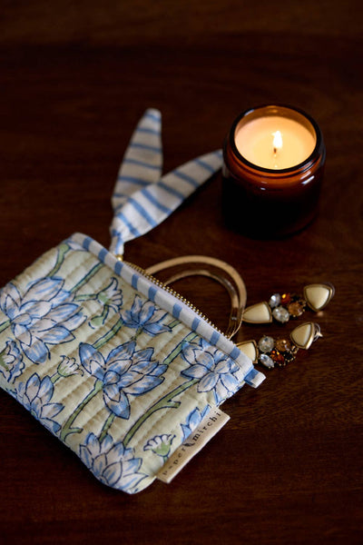 Floral-patterned pouch, earrings and a lit candle on a wooden surface
