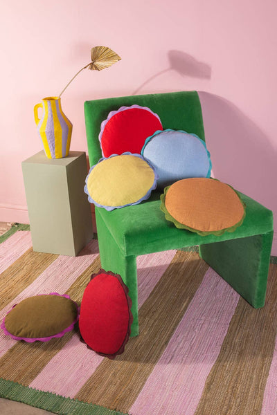 Colourful cushions on a chair  on a striped rug against a pink wall background