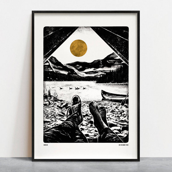 Framed artwork of a people's feet with a view looking out from a tent of a lake with mountains and a gold sun.