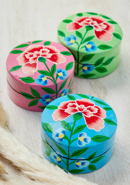 Three colourful round boxes with floral designs on a textured surface.
