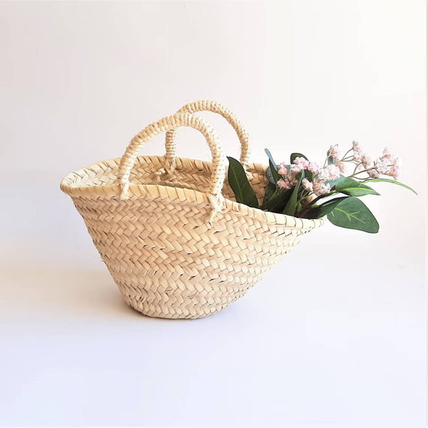 Woven basket with handles holding flowers on a light background