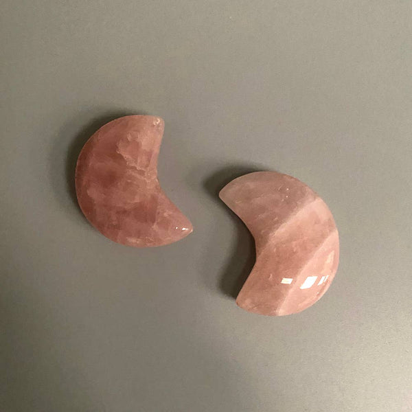 Two pink rose quartz crescent moon-shaped crystals on a grey background