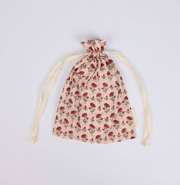 A small drawstring pouch made of light pink fabric with an allover red rose print and cream-colored drawstring ties, laid flat on a light grey background.