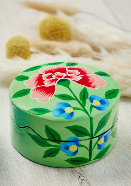 Green round box with floral design on a light wooden surface
