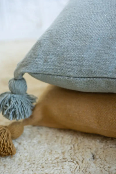 Two textured pillows, one blue with tassels and one mustard yellow, on a light surface.