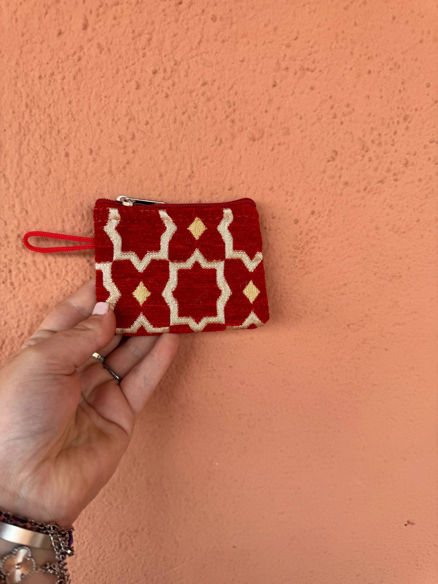Hand holding a red and white patterned pouch against a pink wall