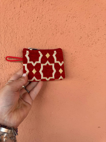 Hand holding a red and white patterned pouch against a pink wall