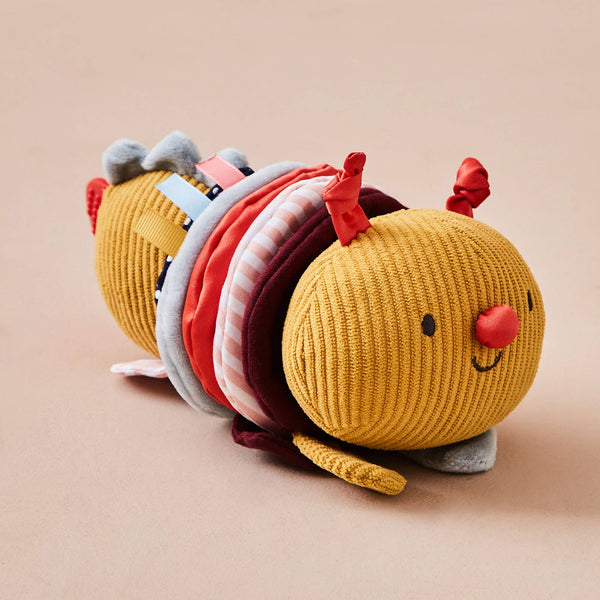 Yellow caterpillar-shaped plush toy with colorful segments on a beige background
