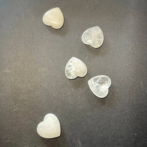Five heart-shaped clear quartz crystals on a dark grey background