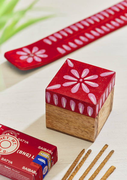 Box with a red and white floral-patterned lid with incense sticks on a light surface