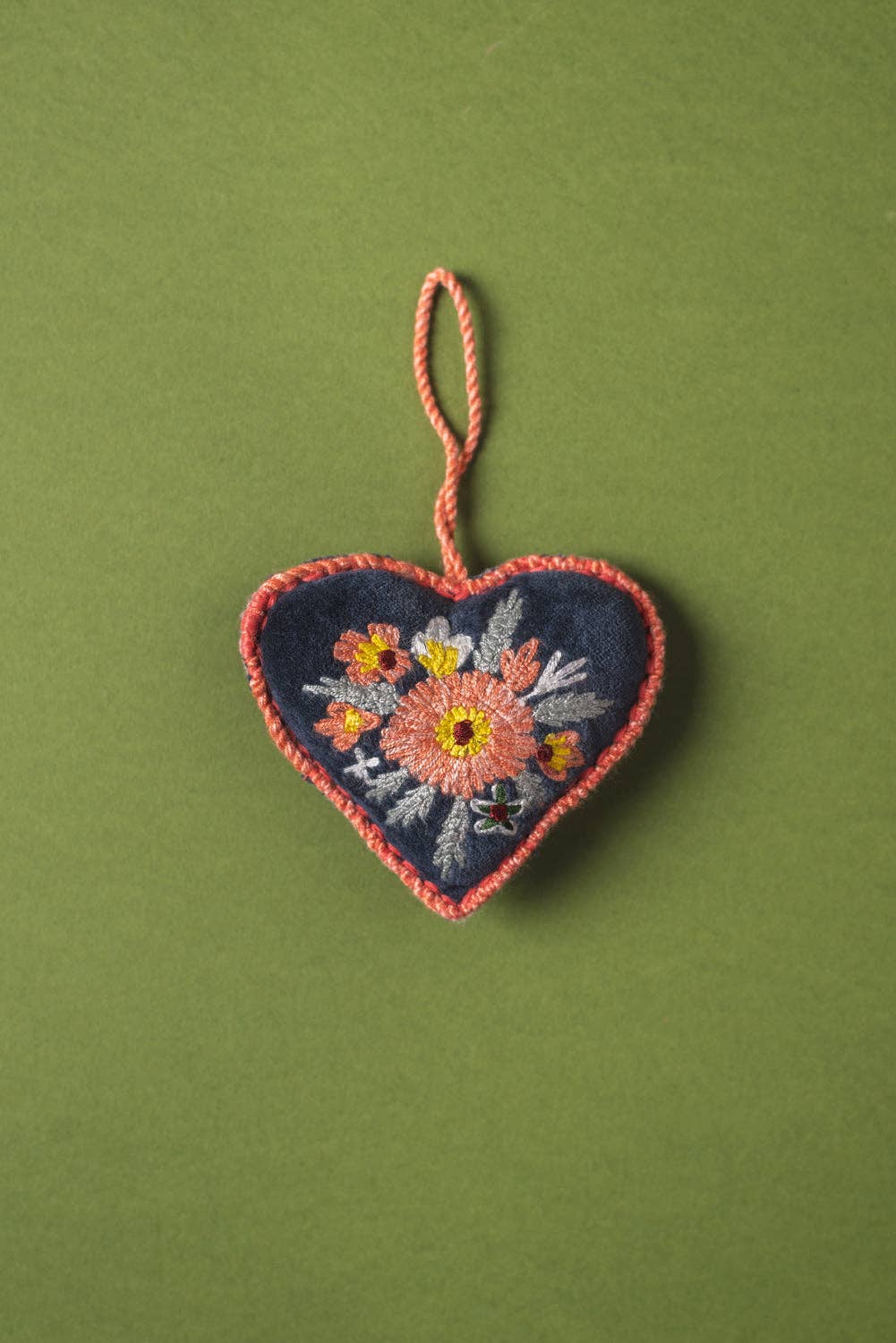 Embroidered heart-shaped ornament with floral design on a green background