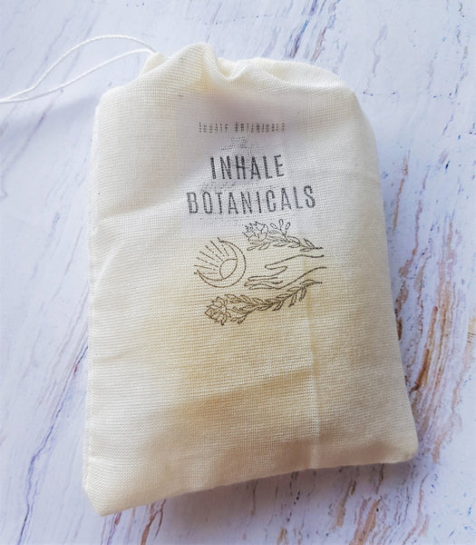Beige drawstring bag with 'Inhale Botanicals' branding on a light wooden surface