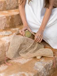 Person taking a bottle of Sol de Ibiza Face & Body Magic Sun Oil ot of a woven bag on stone steps