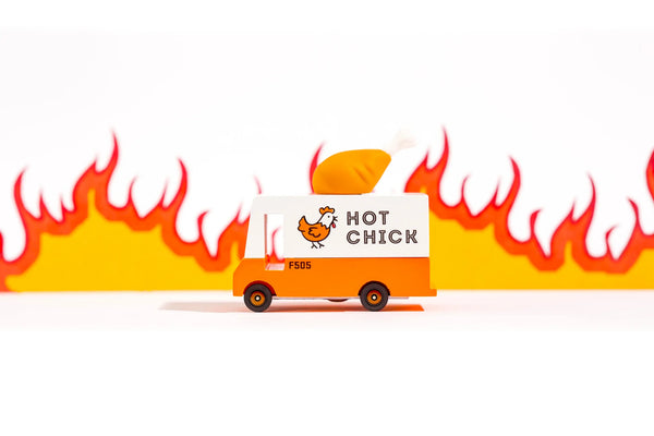 An orange wooden toy van with a 'Hot Chicken' text label and a rubber drumstick topper designed to look like a chicken.against a fiery backdrop