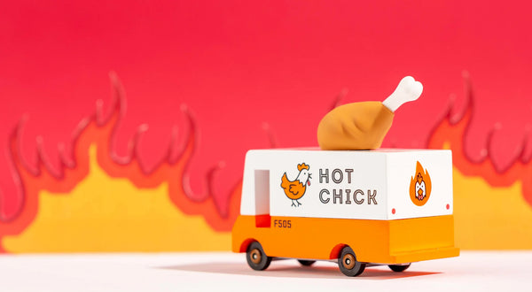 An orange wooden toy van with a 'Hot Chicken' text label and a rubber drumstick topper designed to look like a chicken against a fiery backdrop